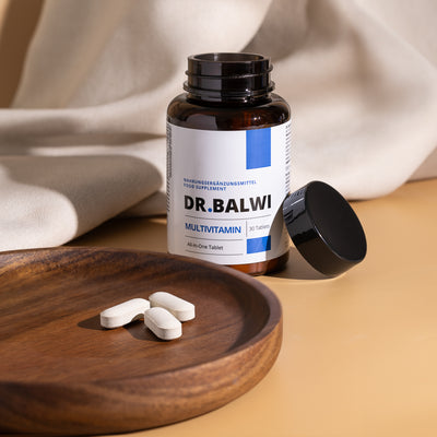 Eine geöffnete Flasche Dr. Balwi Shop Multivitamin Complex mit schwarzem Deckel steht auf einer beigen Fläche, vier weiße Tabletten mit der Aufschrift Zink Immunsystem und Reishi-Pilzextrakt liegen auf einer runden Holzplatte in der Front.