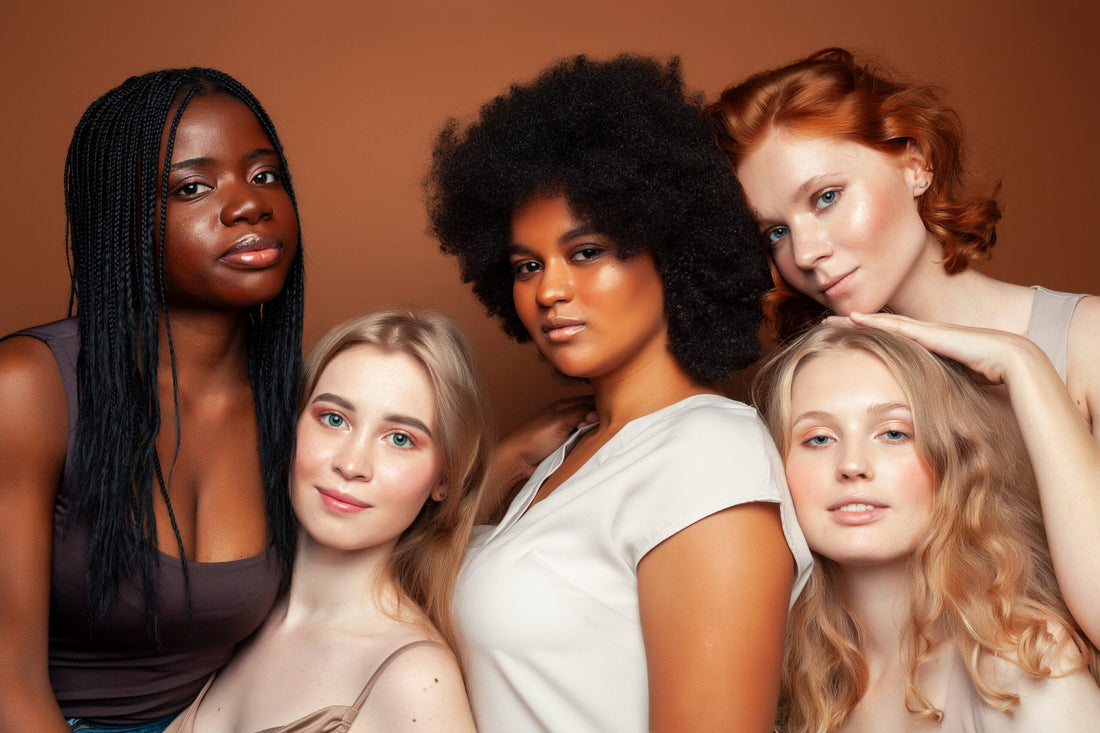 Five women with different hair types, posing together against a brown background.