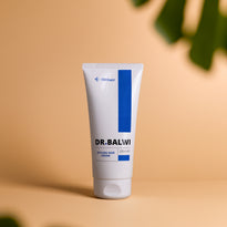 Eine Tube der Dr. Balwi Styling & Repair Creme (200 ml) aus dem Dr. Balwi Shop steht aufrecht auf einer beigen Fläche, mit verschwommenen grünen Blättern im Vorder- und Hintergrund, die an eine von der Natur inspirierte Premium-Haarpflege erinnern.