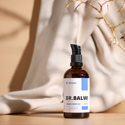 Eine braune Pumpflasche mit der Aufschrift Dr. Balwi Shop Premium Schwarzkümmelöl steht auf einer beigen Fläche mit neutralem Stoff dahinter und getrockneten Pflanzenstängeln auf der rechten Seite, die die Vorteile für die Haut- und Haarpflege, einschließlich der Unterstützung bei Haarausfall, hervorheben.