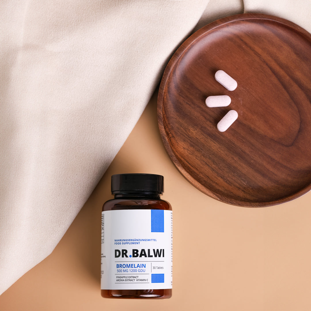Ein Fläschchen Dr. Balwi Shop Bromelain ruht auf beigem Stoff neben einem Holzteller mit drei rosa Tabletten, die die Vorteile von Ananas Extrakt für alle, die von Haarverlust betroffen sind, aufzeigen.