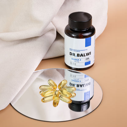 Eine Flasche mit der Aufschrift "Daily Omega 3" aus dem Dr. Balwi Shop steht auf einer beigen Fläche neben einem weichen Stoff. Mehrere gelbe Omega-3-Kapseln, die das Haarwachstum unterstützen und den Haarausfall reduzieren, sind auf einem runden Spiegel davor angeordnet.