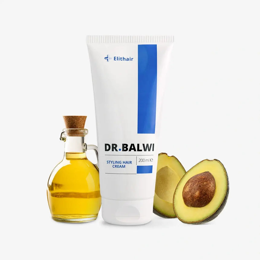Eine Tube der Dr. Balwi Styling & Repair Creme von Dr. Balwi Shop steht neben einer kleinen Glasflasche Arganöl mit Korken und einer halbierten Avocado - ideal für geschmeidiges Haar auf weißem Hintergrund.