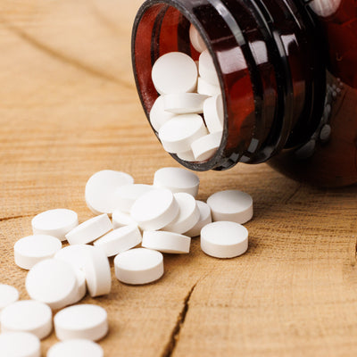 Eine braune Glasflasche aus dem Dr. Balwi Shop liegt umgekippt auf dem Holz und verschüttet kleine, runde weiße Zink-Tabletten, die das Immunsystem und das Haarwachstum unterstützen.